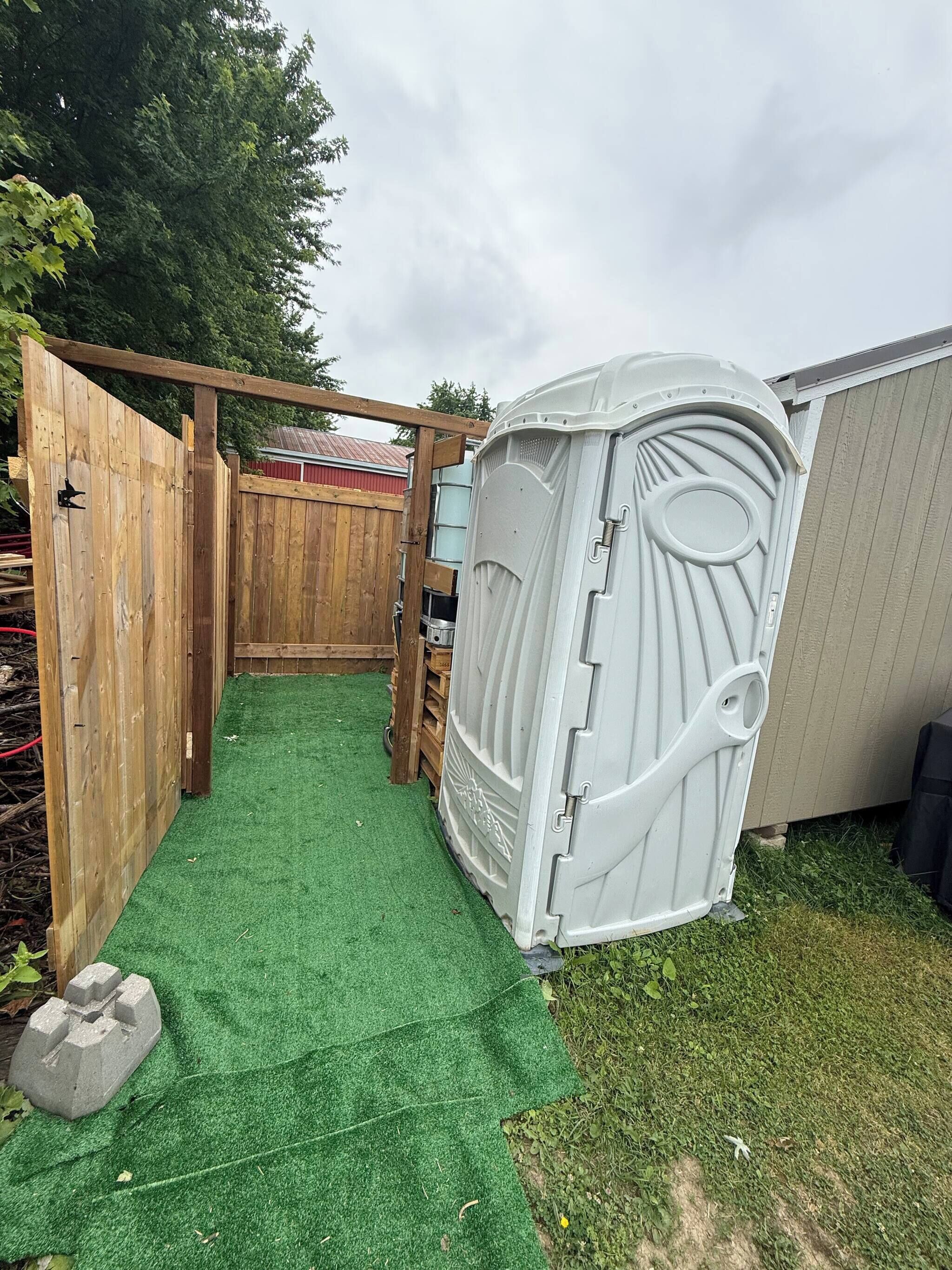 A fenced backyard with artificial turf, a wooden gate, and a white structure with a circular window.