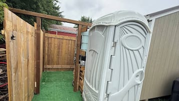 A fenced backyard with artificial turf, a wooden gate, and a white structure with a circular window.