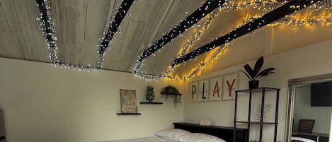 Un dormitorio con cama, sofá marrón, techo decorado con luces y una pared con un cartel que dice 'PLAY'.