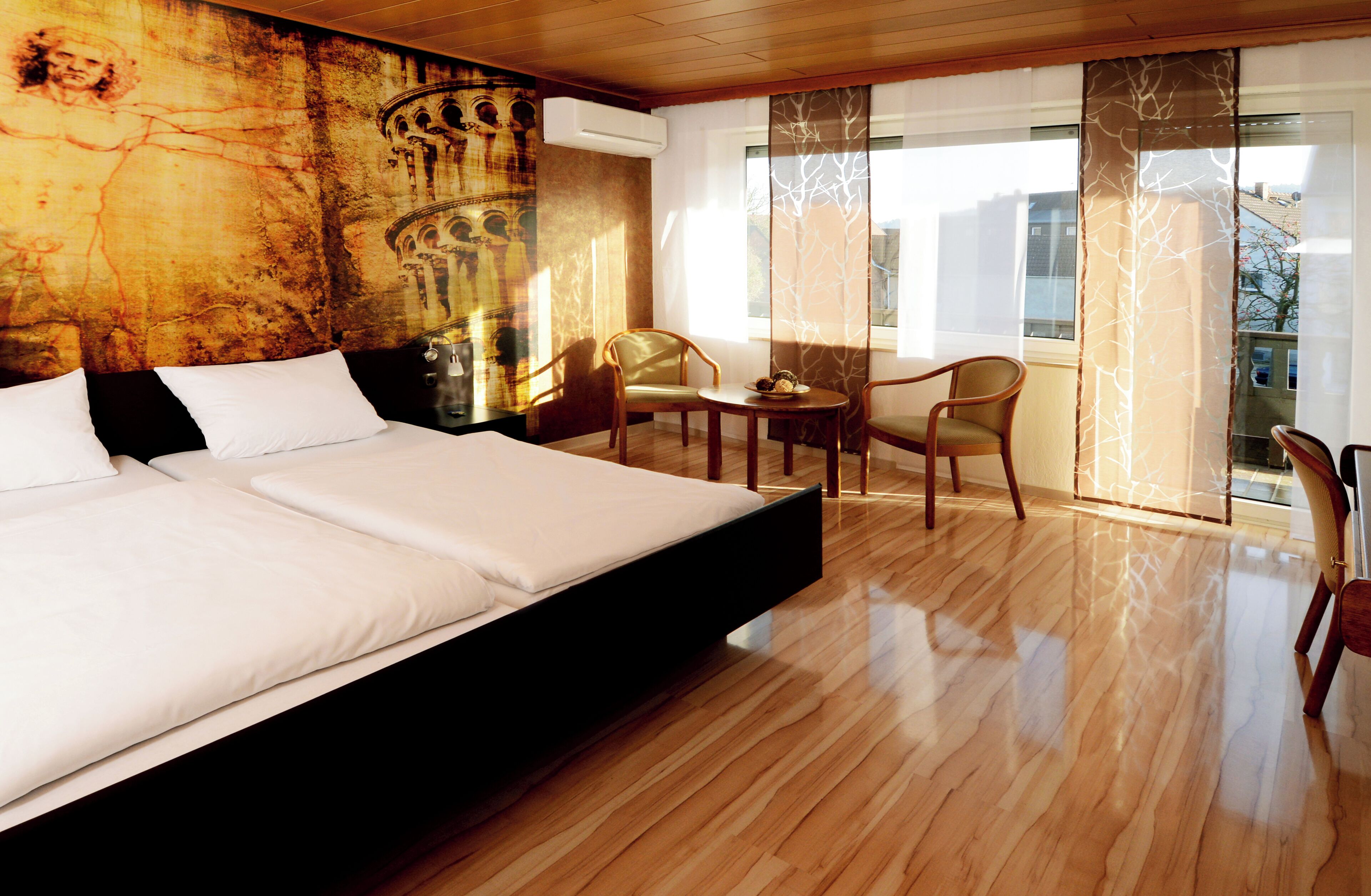 Habitación de hotel con una cama grande, una mesa de comedor, dos sillas, vistas a la ciudad y un mural en la pared.