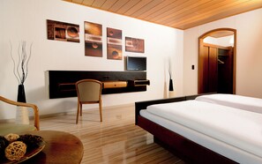 A hotel room with a bed, desk, chair, TV, and artwork on the wall.