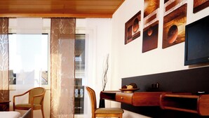 Ein modernes Wohnzimmer mit Holzboden, einer Couch, zwei Sesseln, einem Couchtisch und einem an der Wand befestigten Flachbildfernseher.