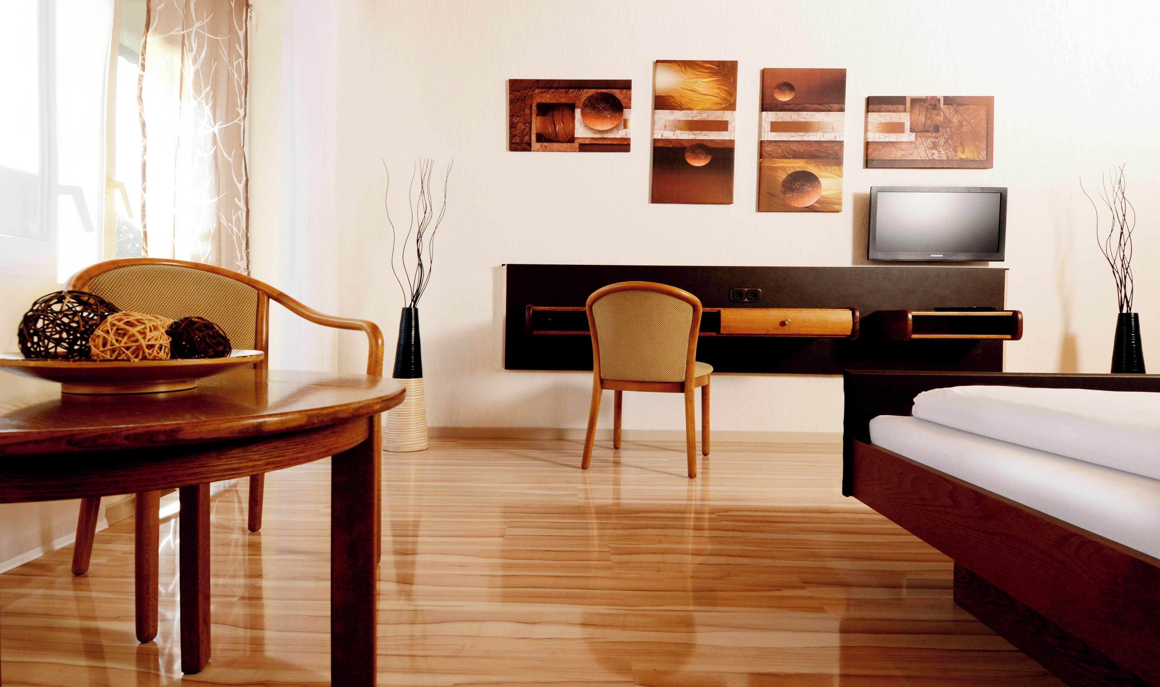 Hotelkamer met houten vloer, een eettafel met fruitschaal, een bank, een televisie en kunst aan de muur.