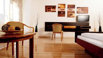 Hotelkamer met houten vloer, een eettafel met fruitschaal, een bank, een televisie en kunst aan de muur.
