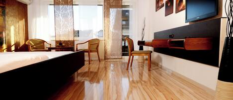 A hotel room with a bed, two chairs, a TV, and a wooden floor.