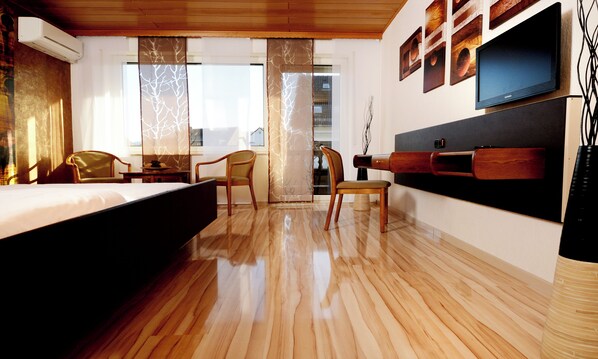 A hotel room with a bed, two chairs, a TV, and a wooden floor.