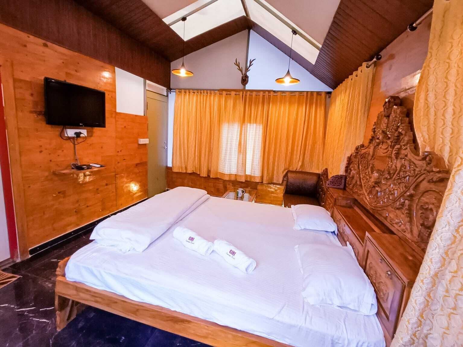 Una cama grande con ropa blanca, un televisor montado en la pared y un techo de madera.