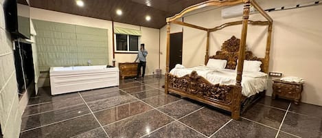 A bedroom with a four-poster bed, a vanity, a dresser, and a large window.