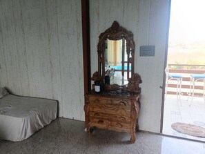 A room with a wooden dresser, a bed, a mirror, and a view of the outside. - Giri Sarovar Resort (Paud)