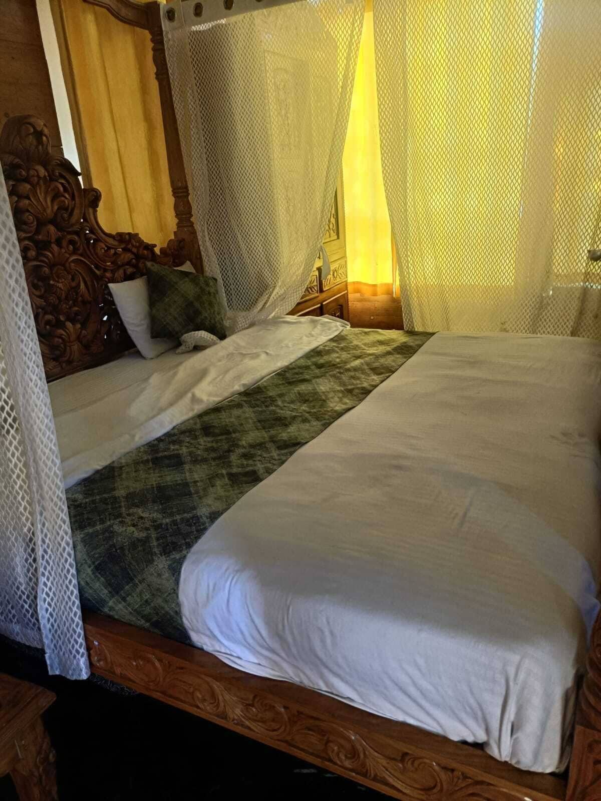 A bed with a canopy, a wooden headboard, and a green throw blanket.