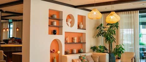 Una sala moderna con un sofá, sillones y una zona de comedor. Hay estanterías con objetos decorativos y una planta grande.