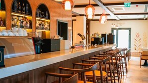 Zona de bar con una barra alargada, varios taburetes e iluminación colgante.