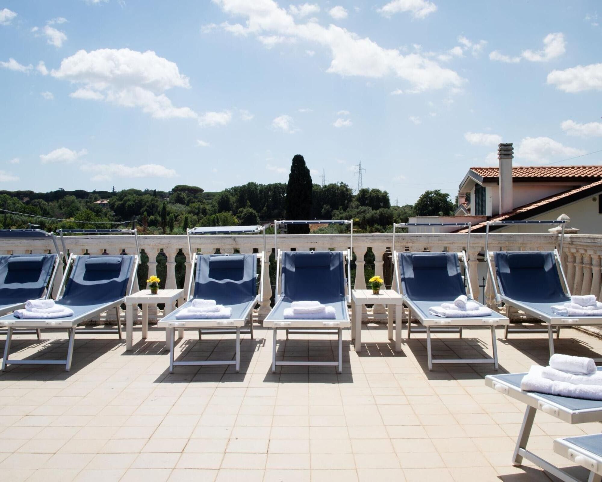 A rooftop terrace with sun loungers, a tiled floor, and a view of the surrounding landscape.