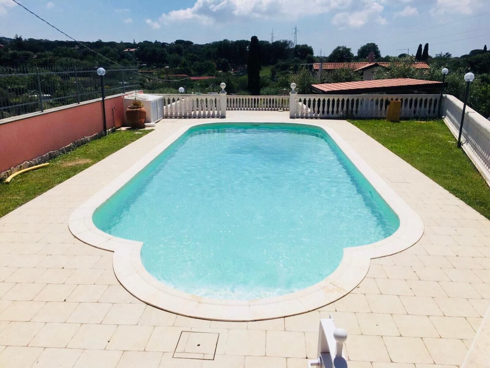 Ein rechteckiger Pool mit weißem Rand, umgeben von einer gepflasterten Liegefläche und einem weißen Zaun.