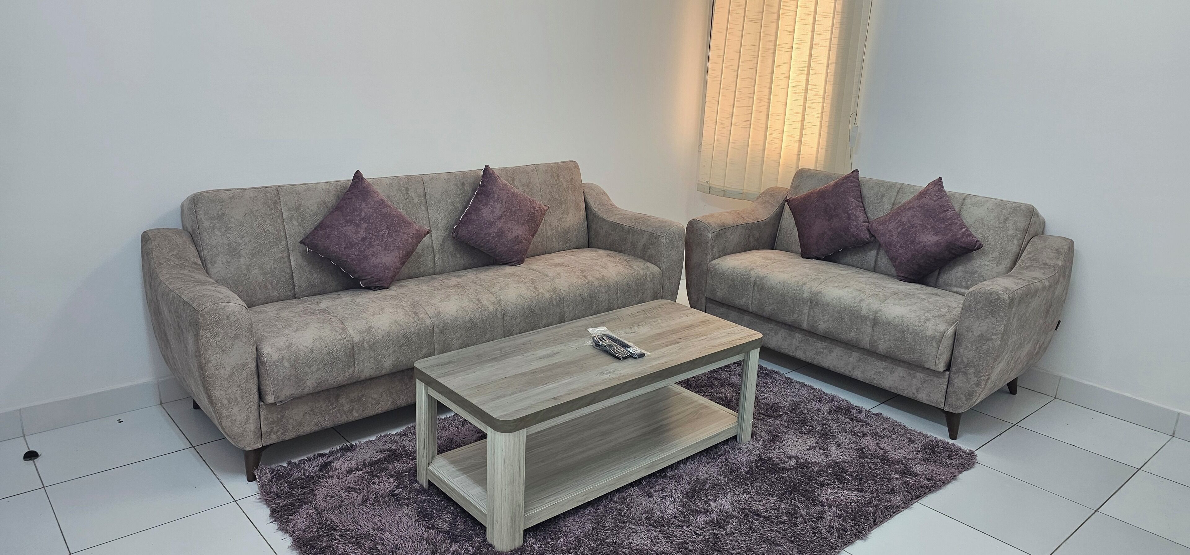 Un salon avec deux canapés gris, une table basse en bois et un tapis violet.