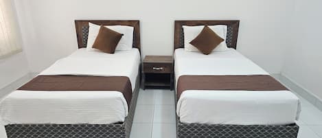 Two twin beds with brown headboards and footboards, a small wooden nightstand between them, and a patterned rug on the floor.
