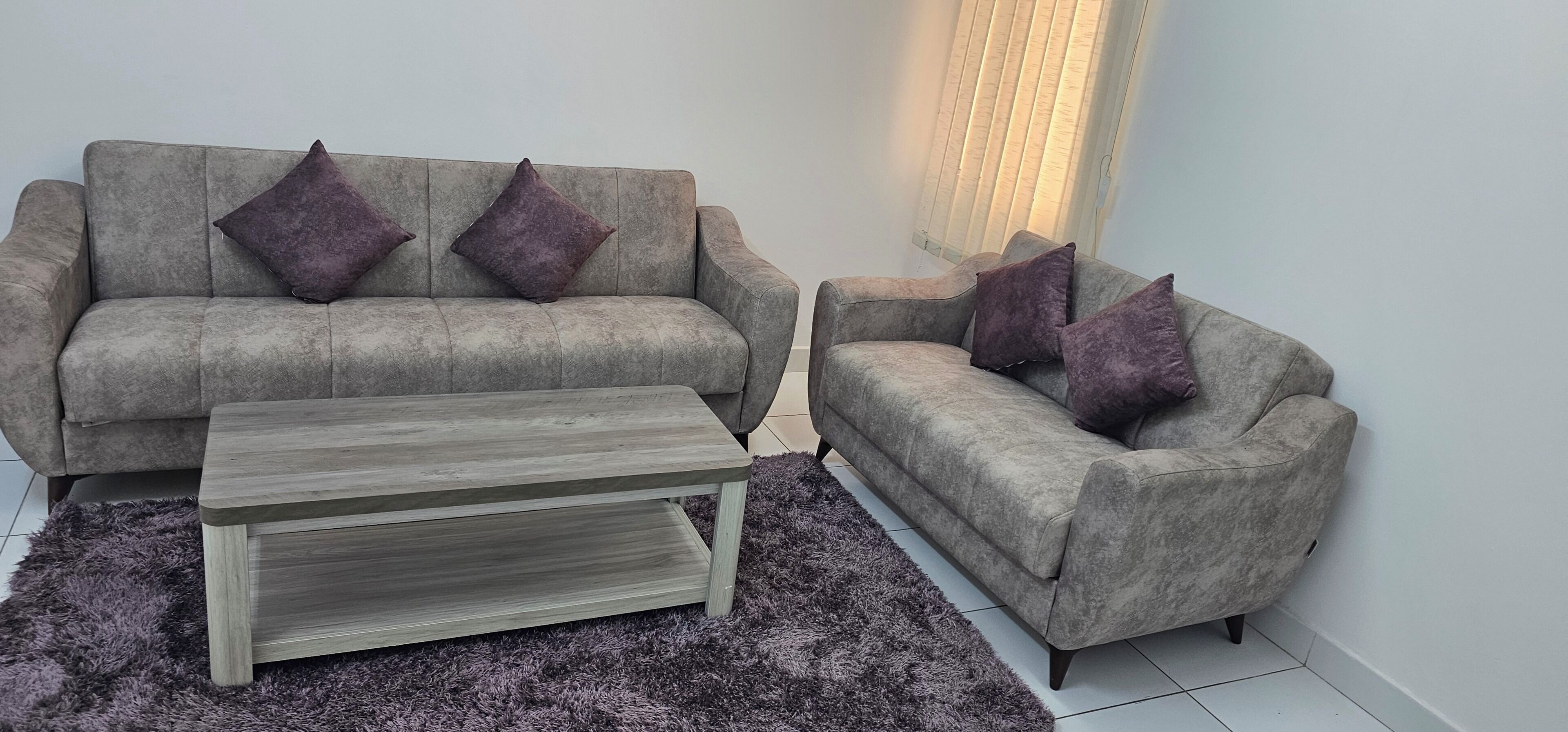 Ein Wohnzimmer mit zwei grauen Sofas, einem Holztisch und einem violetten Teppich.