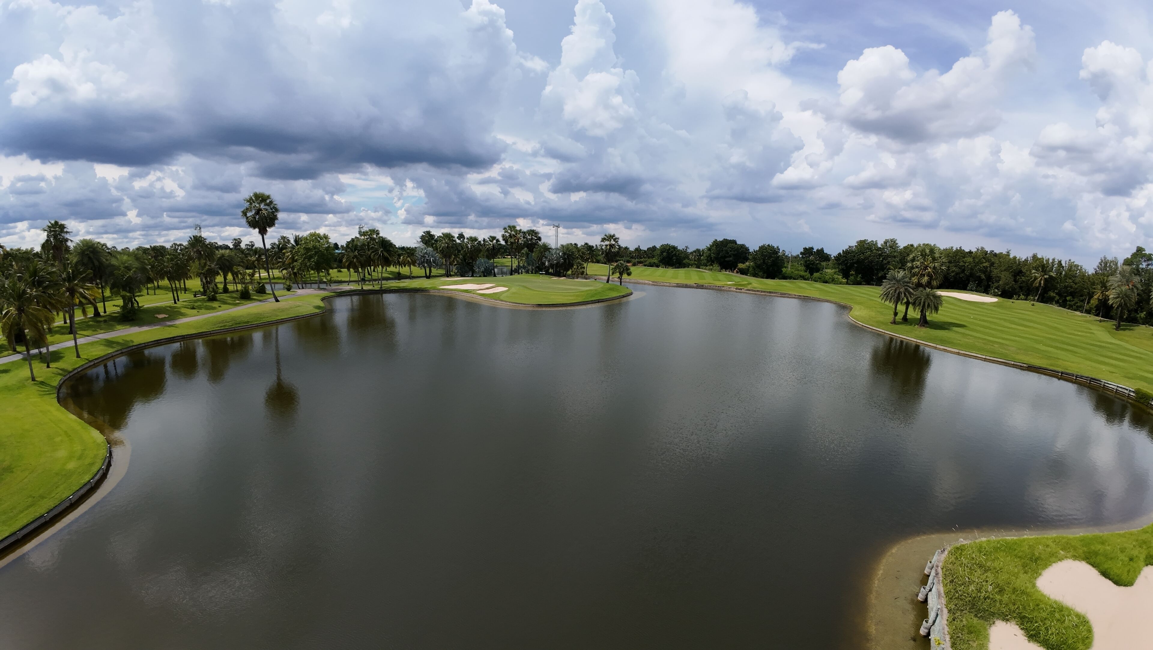 A golf course with a large pond, green fairways, and palm trees.