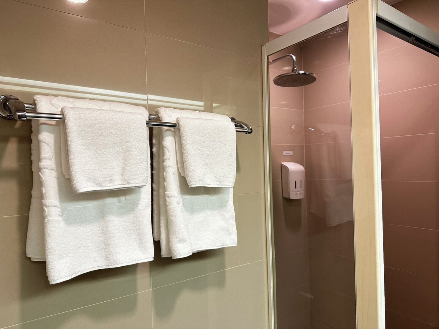 A bathroom with two white towels hanging on a rack, a glass shower enclosure, and a soap dispenser.