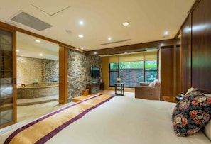 Un dormitorio con una cama grande, una pared de piedra, un televisor, una ventana y un baño con pared de piedra y un lavamanos.