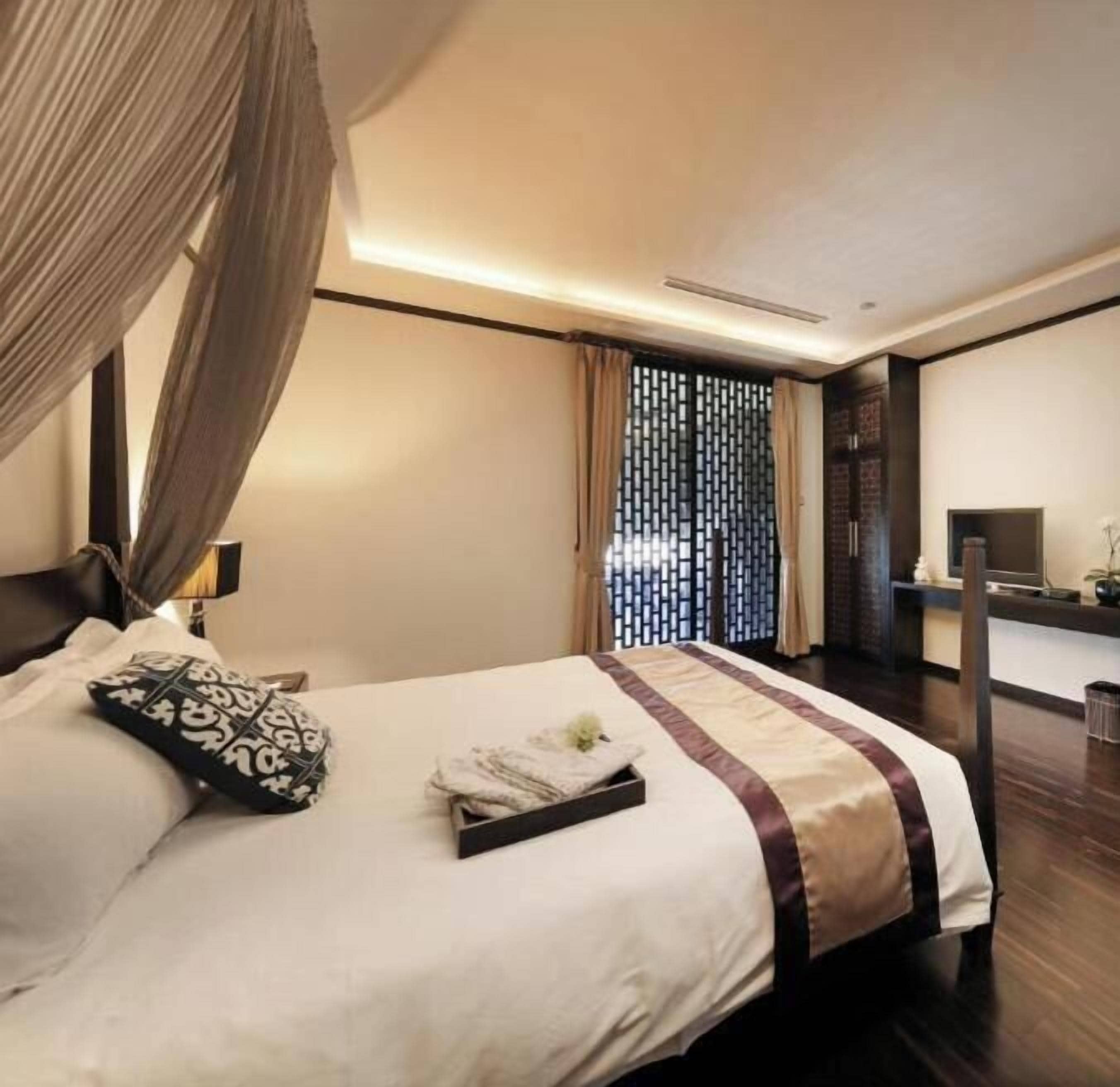 A hotel room with a bed, curtains, a desk, and a TV.
