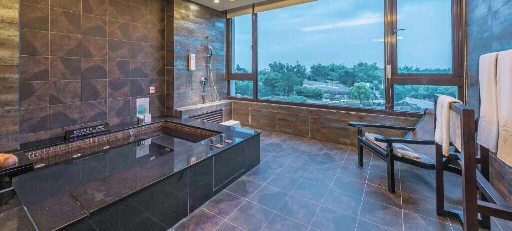 A modern bathroom with a large bathtub, a shower area, and a seating bench.