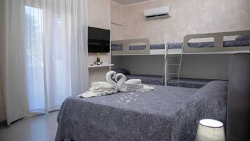 Ein Hotelzimmer mit Etagenbetten, einem Fernseher, einer Minibar und einem Fenster mit durchsichtigen Vorhängen.