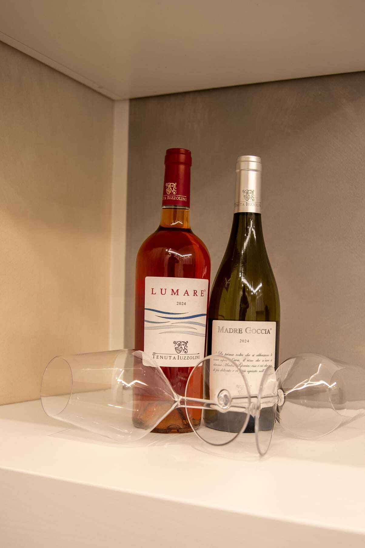 Two wine bottles on a shelf with a pair of glasses.