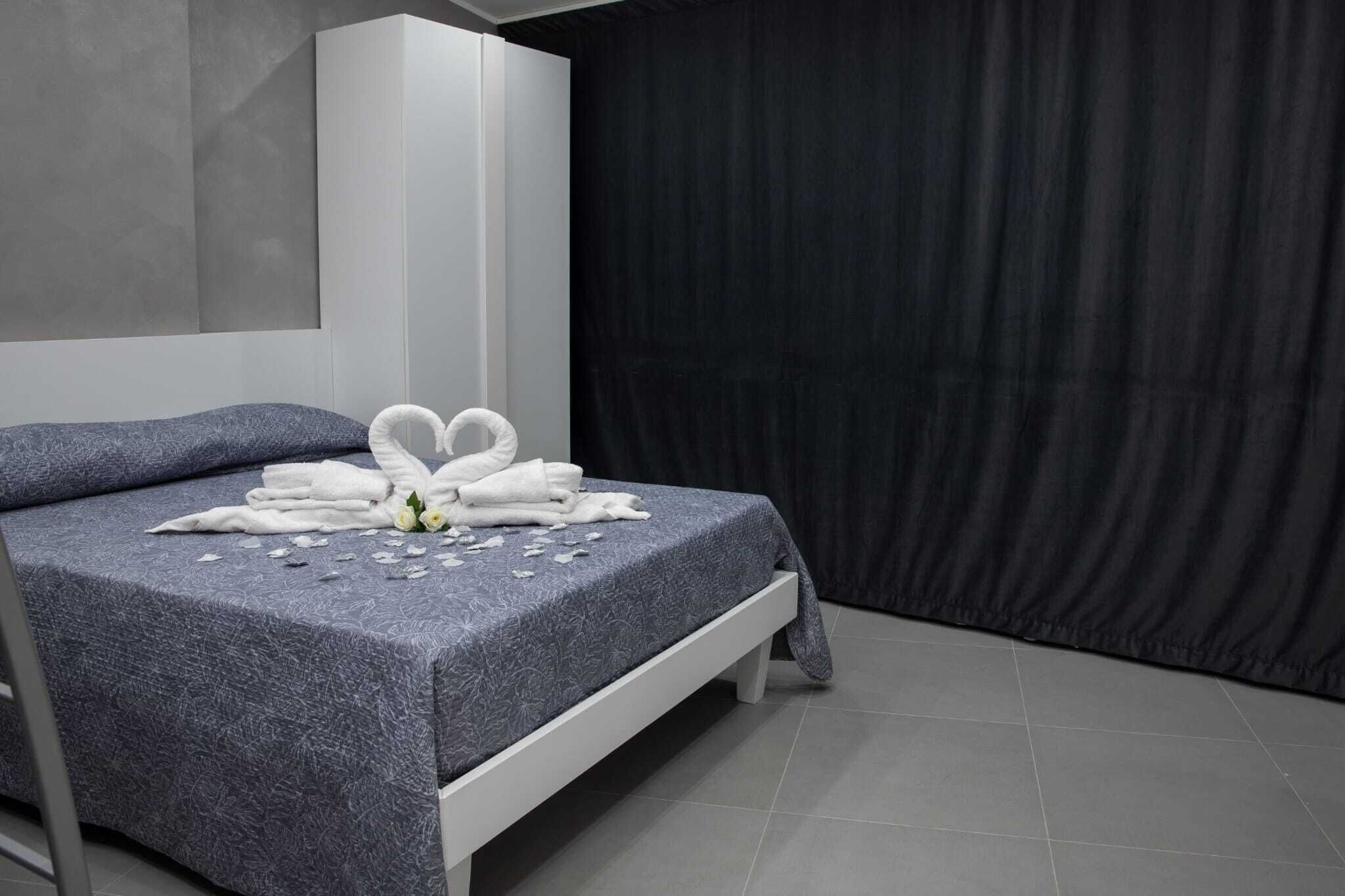 A neatly made bed with towels and a flower arrangement, a dark curtain, and a modern room design.