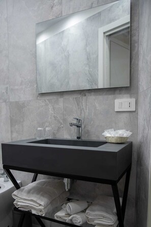 Un baño con un lavamanos rectangular, un espejo encima y un perchero debajo.