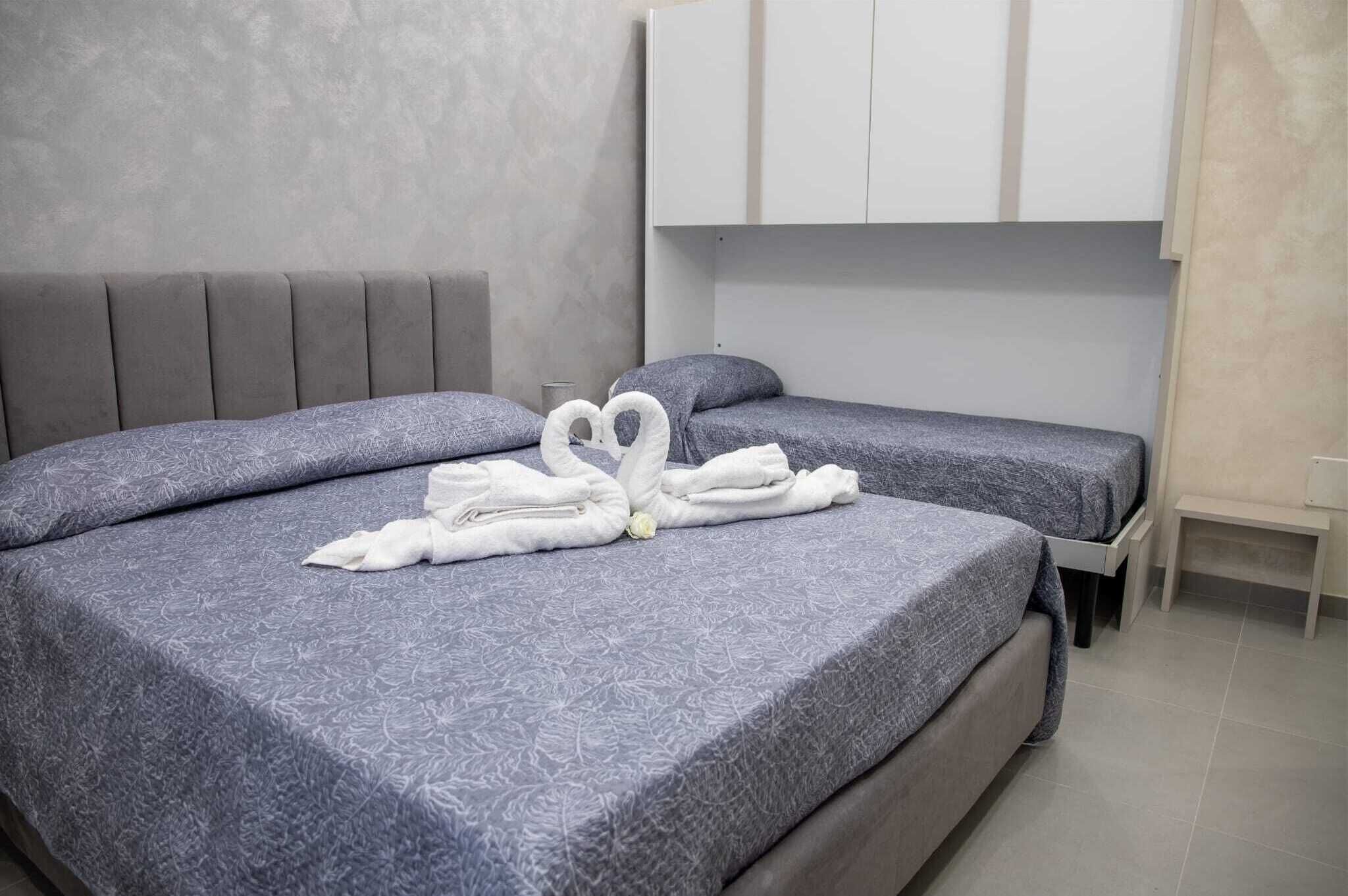 Ein Hotelzimmer mit zwei Betten, grau gemusterten Bettbezügen, einem grauen Kopfteil und einer weißen Wand mit einem Schrank.