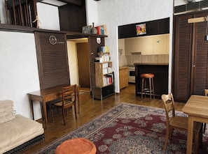 A living room with a wooden floor, a sofa, a coffee table, a rug, a bookshelf, and a kitchen area with cabinets and a countertop. - Artist Studio by the Lake (Genève)