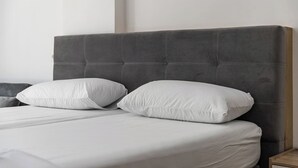 A bed with a grey upholstered headboard, two white pillows, and a wooden nightstand. - Sea & Stay Studio | Durrës Waterfront by PikHost (Durrës)