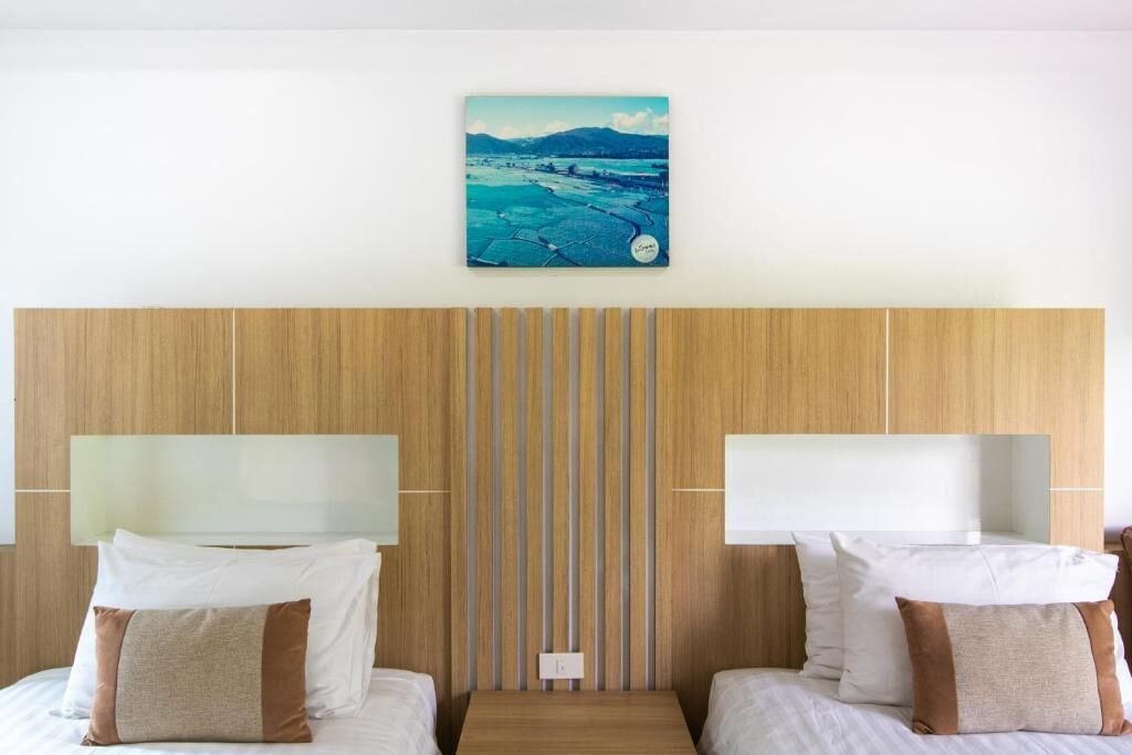 Ett hotellrum med två sängar, en sänggavel i trä, en tavla ovanför sängarna och en väggmonterad lampa.