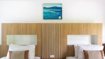 Ett hotellrum med två sängar, en sänggavel i trä, en tavla ovanför sängarna och en väggmonterad lampa.