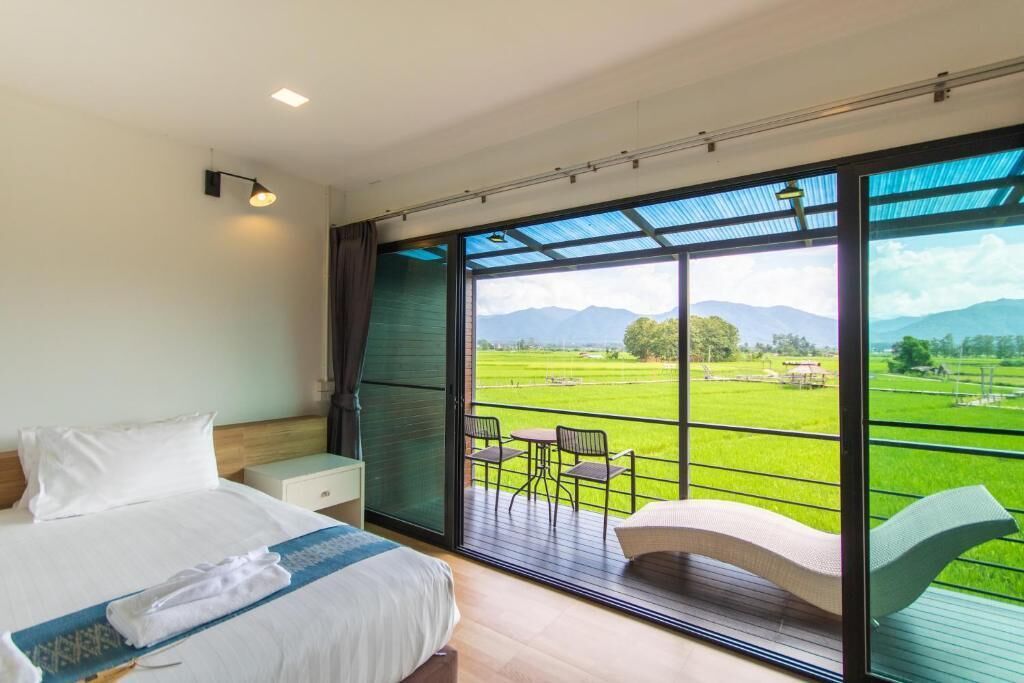 A bedroom with a large window, a bed, a nightstand, and a view of a green landscape.