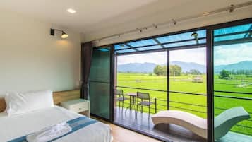 A bedroom with a large window, a bed, a nightstand, and a view of a green landscape.