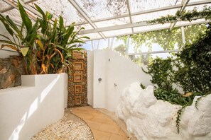 Un espacio al aire libre cubierto con un muro de piedra, una pared blanca con vegetación y un sendero.