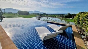 Una piscina infinita con sillones de descanso, rodeada por un jardín ajardinado y vistas a montañas distantes.