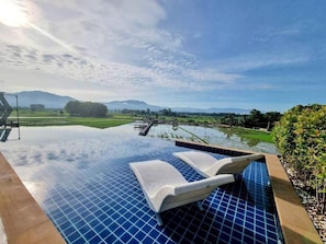An infinity pool with lounge chairs, surrounded by a landscaped garden and a view of distant mountains. - Sangthong Resort (Chiang Klang)