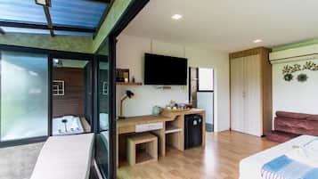A modern room with a desk, a television, a bed, and a sliding glass door leading to a balcony.
