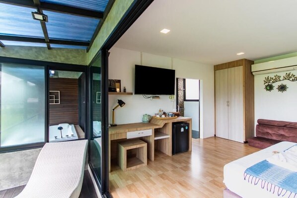 Una habitación moderna con escritorio, televisión, cama y puerta corrediza de vidrio que da a un balcón.