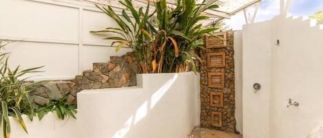 A covered outdoor area with a white wall, a stone wall with wooden panels, and a wooden staircase leading to a door.