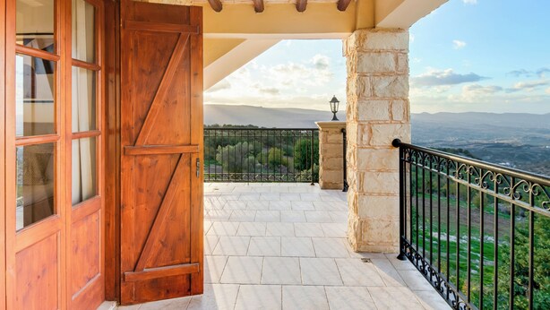 A balcony with a stone pillar, a wooden door, and a view of the landscape. - Sea-view Retreat - Villas With Private Pools (Peristerona)