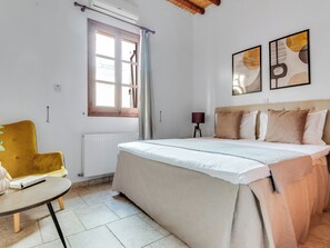 A bedroom with a bed, a window, a radiator, a chair, and artwork on the wall.