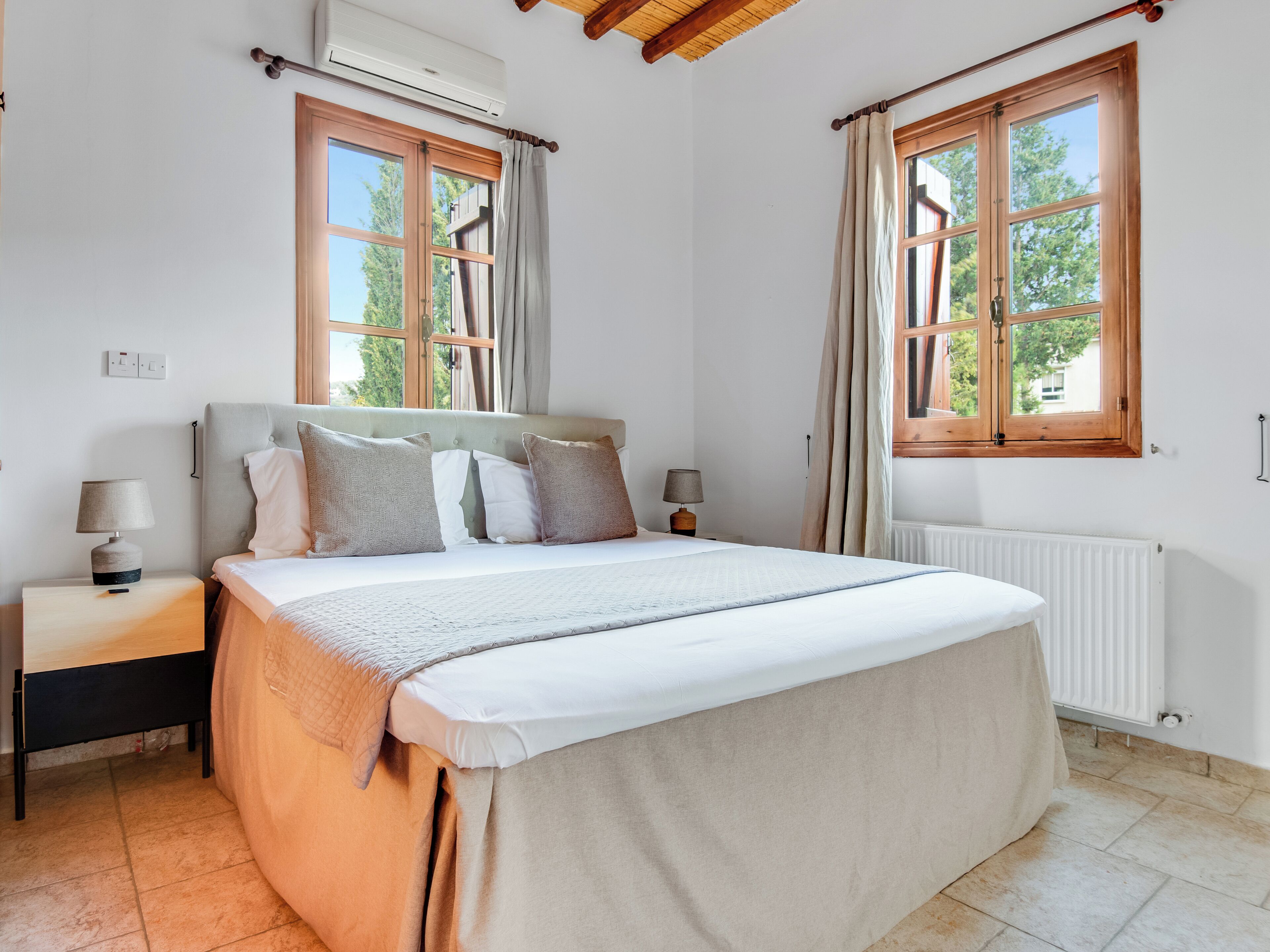 Un dormitorio con cama, dos mesitas de noche, una ventana y un equipo de aire acondicionado.