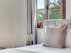 Een slaapkamer met een bed, een raam met gordijnen en een lamp.