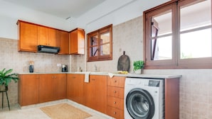 A kitchen with wooden cabinets, a washing machine, a coffee maker, and a potted plant. - Sea-view Retreat - Villas With Private Pools (Peristerona)
