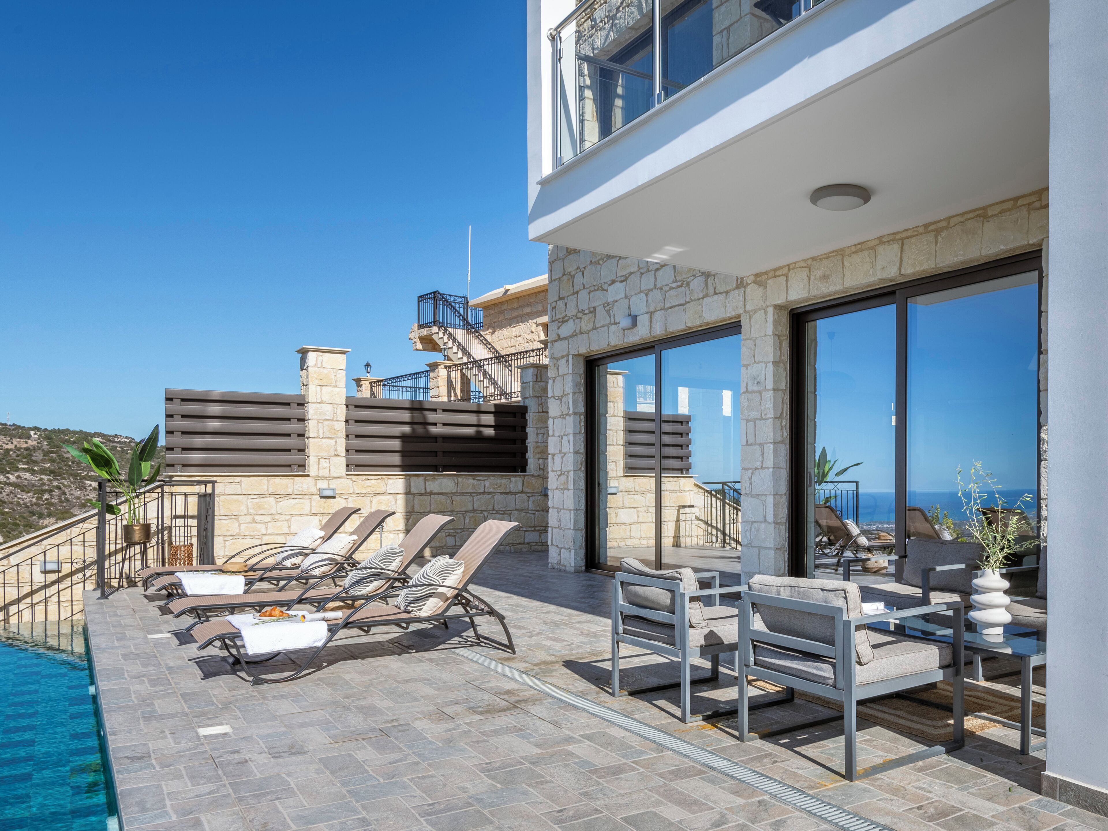 A modern outdoor lounge area with a pool, stone walls, and a view of the sea.
