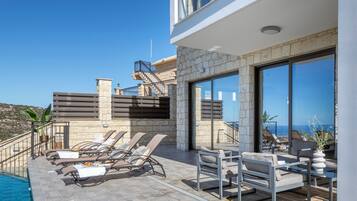 A modern outdoor lounge area with a pool, stone walls, and a view of the sea.